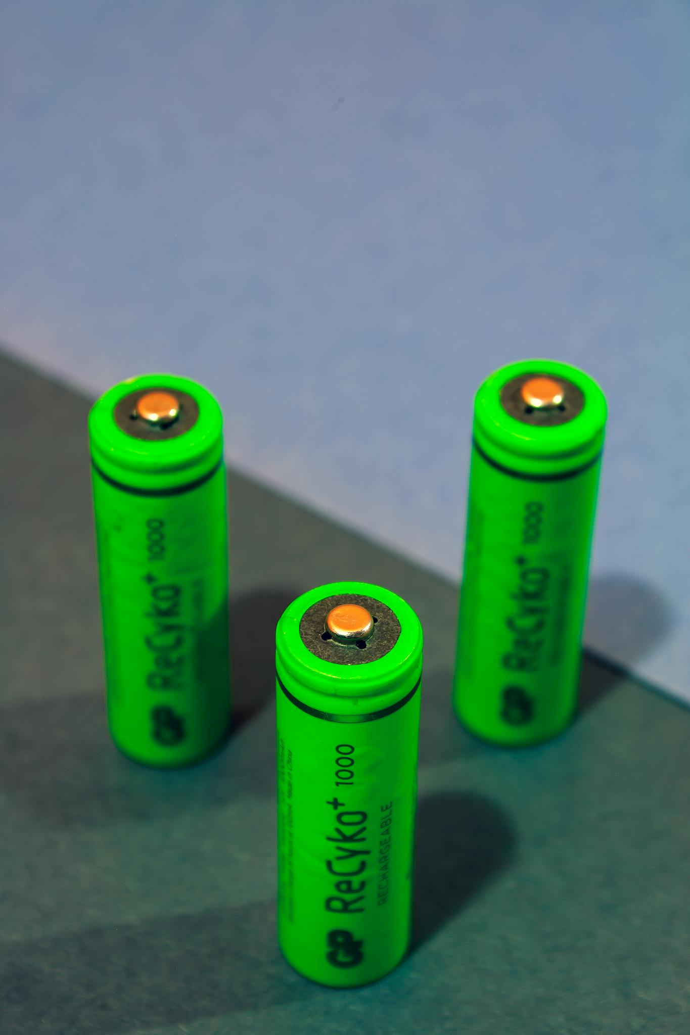 Close-up of three green rechargeable batteries standing on a colored surface.