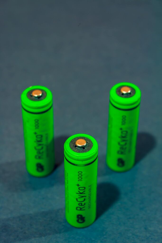 Close-up of three green rechargeable batteries standing on a blue surface.