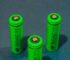 Close-up of three green rechargeable batteries standing on a blue surface.