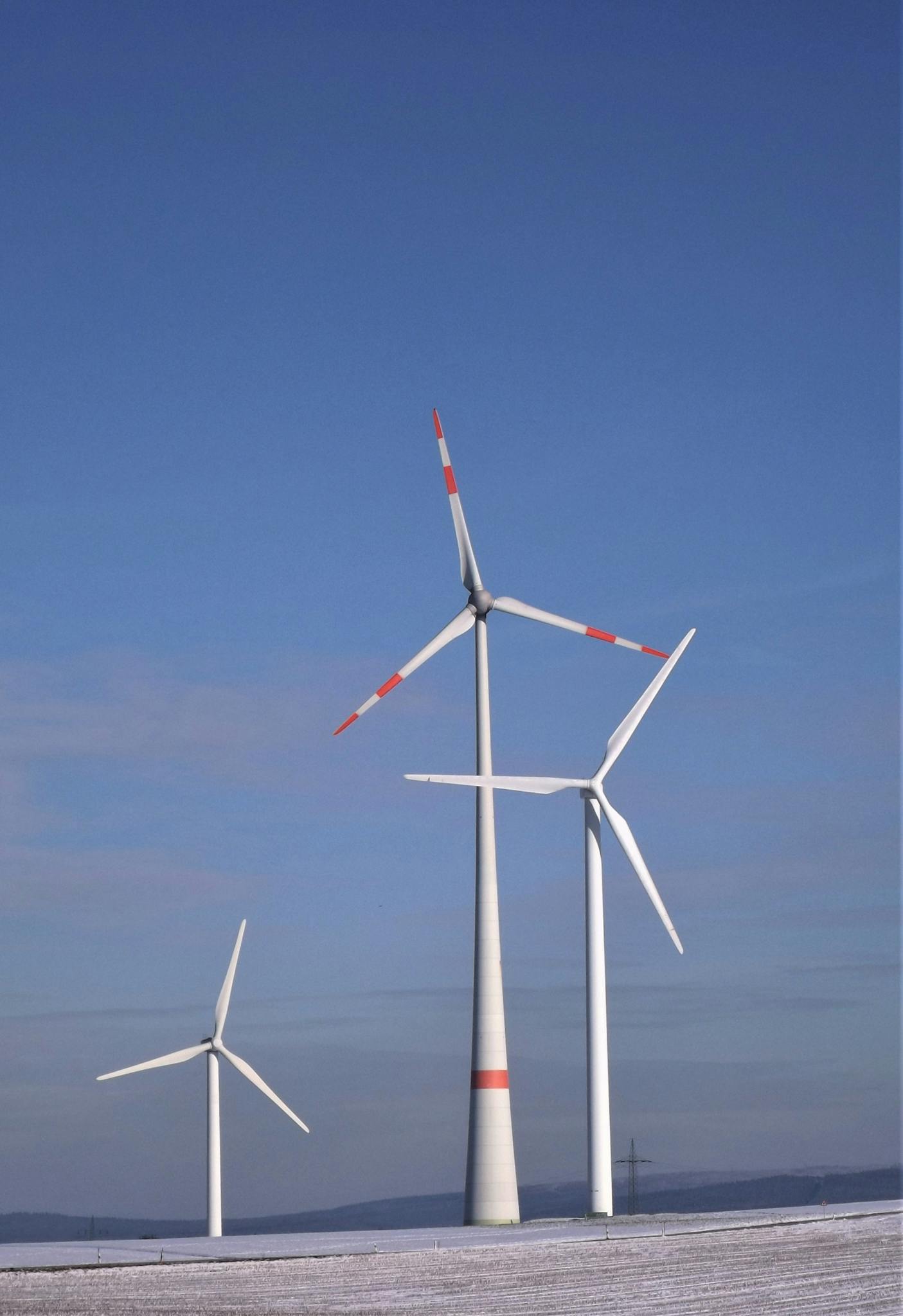 Wind turbines generating clean energy against a clear blue sky in a snowy landscape.
