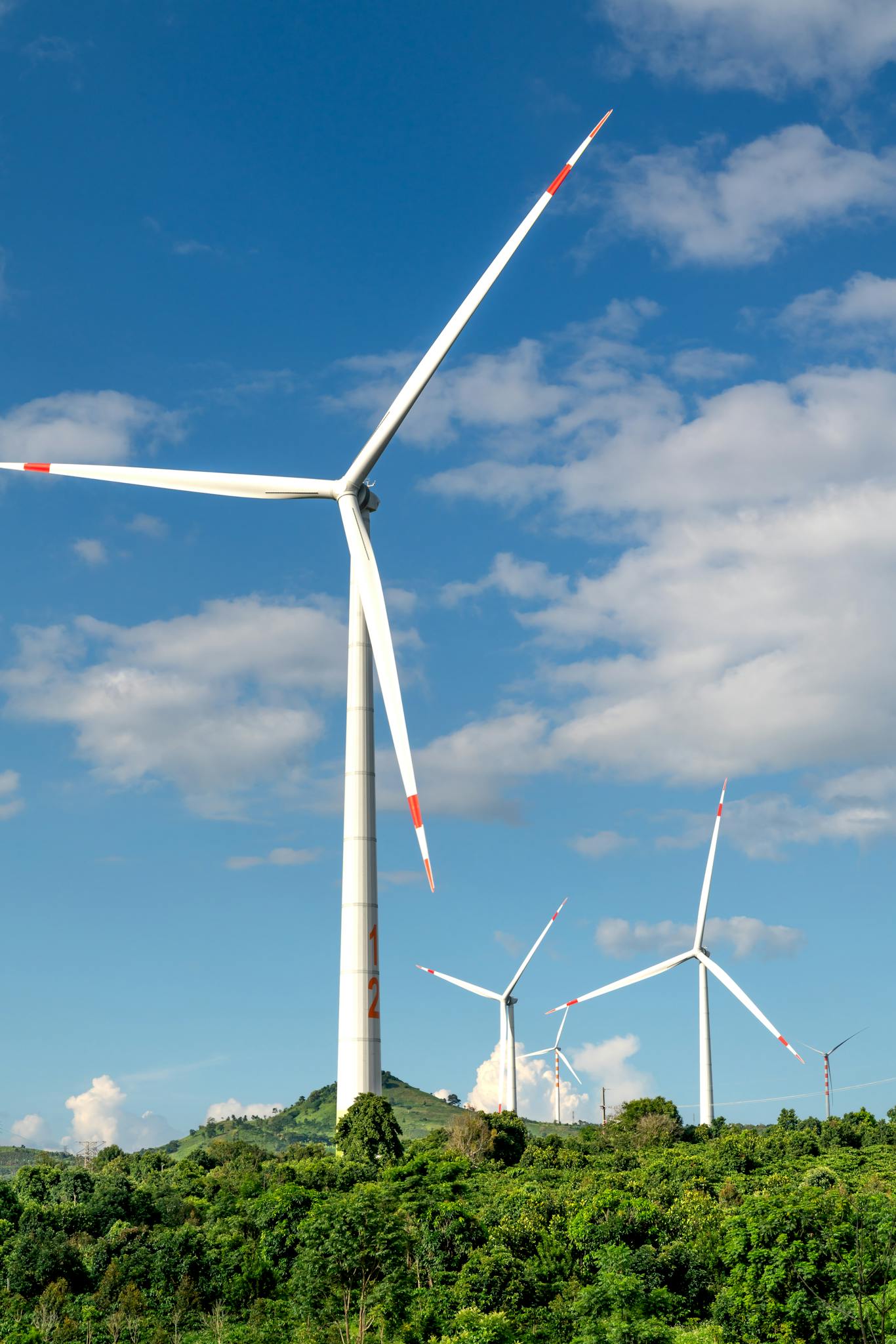 Wind turbines generating renewable energy on a lush green hilltop under a clear blue sky.